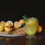 1-2 Taste IFF Lemon Yellow H 6896 Colour displayed as fresh lemon juice in a glass with sliced lemons on a wooden board