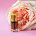 1-2 Taste CEC - Citro Buzz Fragrance displayed as luxurious perfume bottle with a golden cap placed in front of a large, pale peach rose on a pink background
