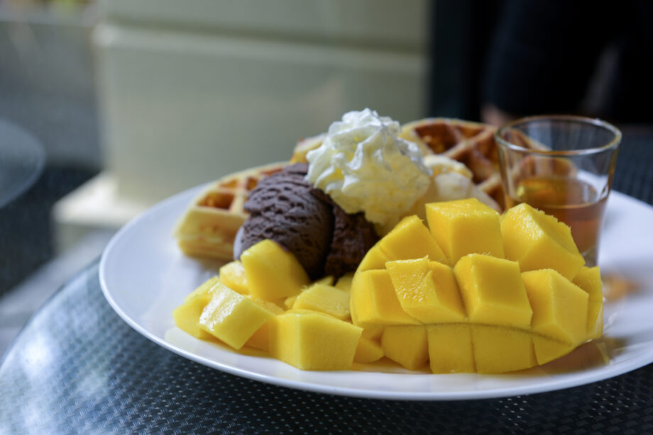 Ripe mango, ice cream, waffles and honey in white dish.