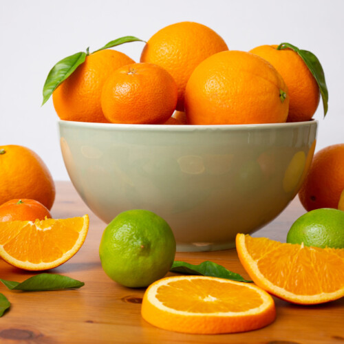 1-2 Taste IFF - Brazil Orange Fragrance displayed as fresh oranges, limes, and tangerines in and around a bowl on wooden table