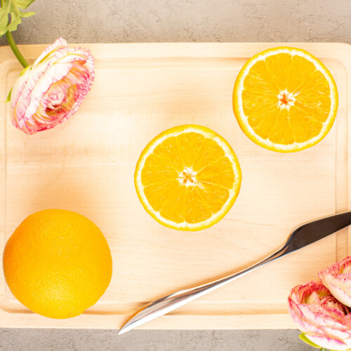1-2 Taste IFF - Lemon Rose Fragrance displayed as fresh orange slices on a wooden tray with soft pink ranunculus flowers