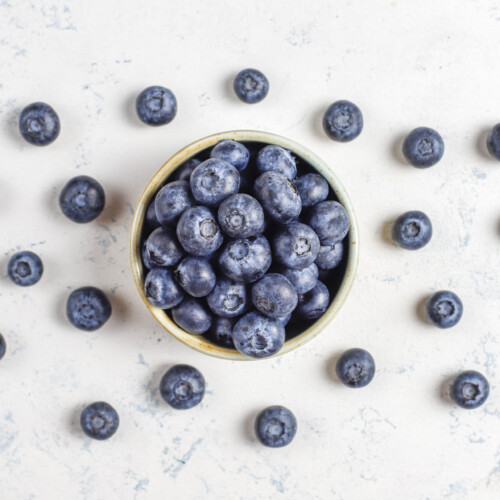 1-2 Taste IFF - Berry Fragrance displayed as ripe blueberries in a bowl with scattered berries on a white textured surface