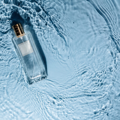 1-2 Taste IFF - Jaspour Modified Fragrance in a clear glass bottle with a golden cap, floating gracefully on rippling blue water