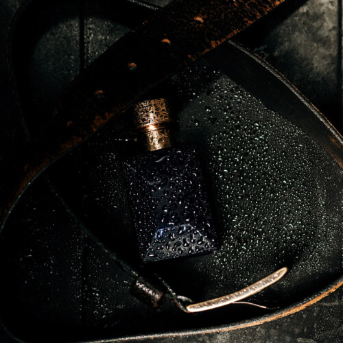 1-2 Taste IFF - Space Clean Fragrance featured in a dark navy glass bottle with golden cap, covered in water droplets and placed on black leather with a vintage belt for a rugged, masculine aesthetic