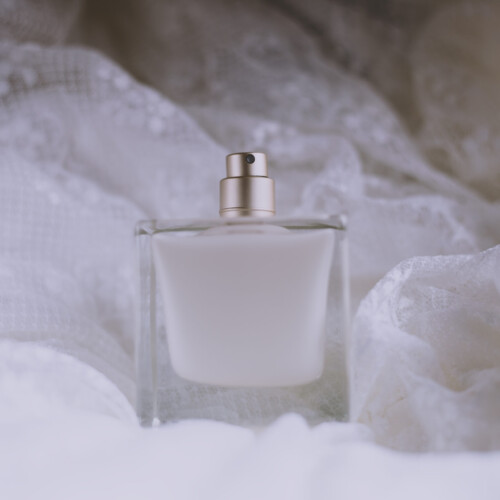 1-2 Taste IFF - Sweet Dreams Fragrance displayed in a frosted white glass bottle with a metallic sprayer, placed on delicate lace fabric