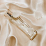 1-2 Taste IFF - Triple Shine Fragrance displayed in a sleek transparent glass bottle with a silver sprayer, elegantly laid on champagne satin fabric with white rose petals