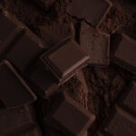 1-2 Taste Campco - Dark Chocolate shown as chunks of dark chocolate bars scattered over cocoa powder
