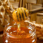 1-2 Taste IFF - Honey Flavour - S 3723 displayed as honey being drizzled from a wooden dipper into a glass jar with a woven basket in the background
