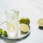 1-2 Taste IFF - Lime Juice & Soda Flavour - S 224 displayed as refreshing lime drink with ice cubes and mint served in a tall glass, garnished with lime slices on a white plate