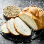 1-2 Taste IFF - Malt Extract Flavour - S 489 displayed as freshly baked round loaf of white bread with sliced pieces on a dark surface, accompanied by a bowl of whole grains