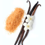 1-2 Taste CEC - Vanilla Powder Flavour - 4979 displayed as vanilla beans with delicate white vanilla flowers and a mound of brown sugar crystals on a white background