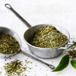 1-2 Taste Australian Native Products – Conventional Lemon Myrtle Dried Leaf Coarse Cut shown as dried green herbs in metal scoops with fresh leaves beside