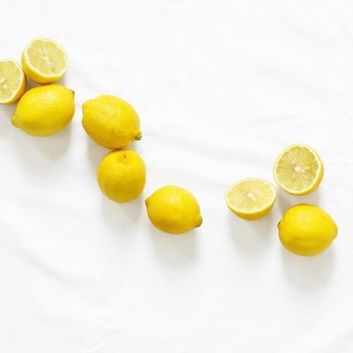 1-2 Taste Aroma INC - Natural Lemon Flavour - O20211 shown as Whole and halved fresh lemons scattered on a white background