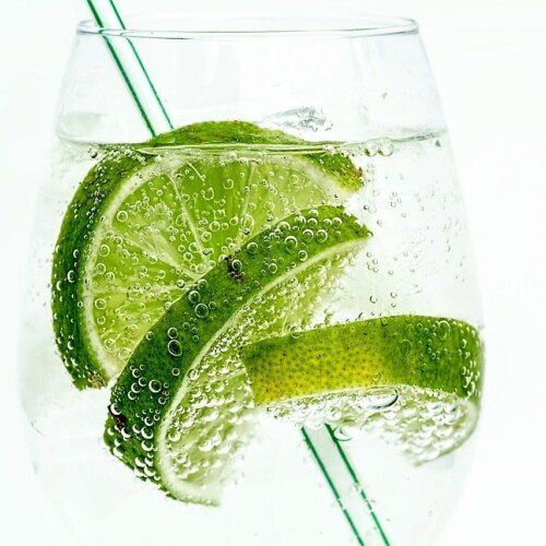 1-2 Taste Aroma INC - Natural Lime Flavour - O20210 shown as Sparkling drink with fresh lime slices and green straw in a clear glass on white background