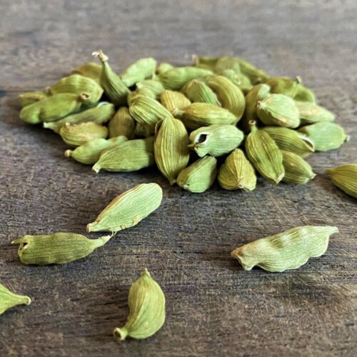 1-2 Taste Aroma INC - Natural Cardamom Extract - O20221 shown as Green cardamom pods scattered on a rustic wooden surface