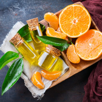 Gesundheit Schönheit Stillleben Konzept ätherisches Bio-Mandarine Mandarine Clementinenöl kleines Glasgefäß mit grünen Blättern Orangenfrucht Grunge-Tisch skaliert