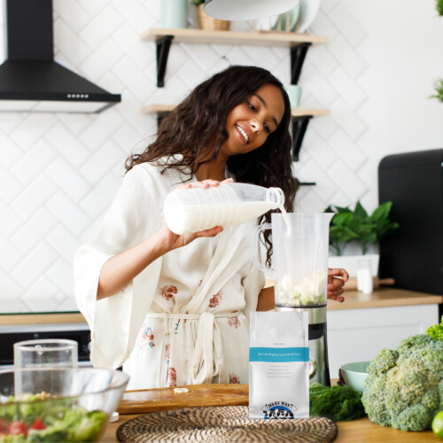 Best Way Ingredients Whey Protein Concentrate (80%) – Woman preparing a healthy smoothie in a blender with milk and vegetables, product pouch visible on kitchen counter
