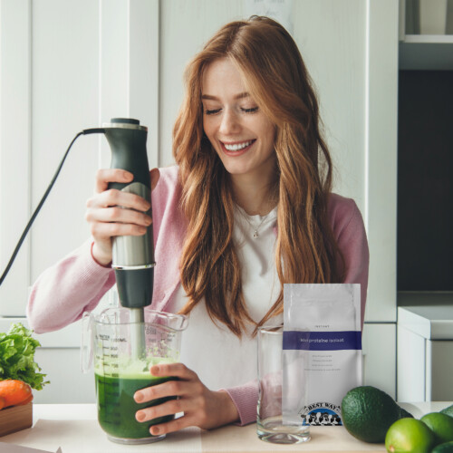 Best Way Ingredients Whey Protein Isolate – Woman blending a green smoothie with fresh vegetables on kitchen counter, promoting healthy lifestyle nutrition