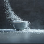 1-2 Taste Nedmag - Calcium Chloride Prills Food Grade shown as Fine White Granules Pouring into Ceramic Bowl on Dark Surface