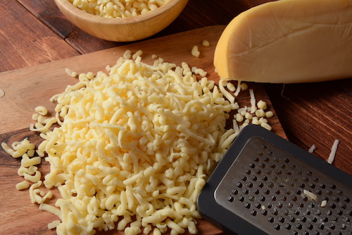 Heap of shredded cheese on small wooden board. Grated cheese for cooking on a cutting board on a wooden background