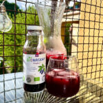 Nutracevit - Organic haskap berry juice NFC bottle with glass and pitcher on outdoor table