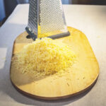 1-2 Taste Trigona - White Cheddar grated into fine shreds on wooden board with metal grater