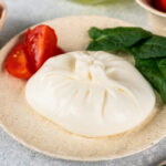 1-2 Taste Trigona - Burrata di Bufala on plate with fresh spinach and cherry tomatoes, creamy Italian cheese with delicate texture