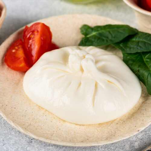 1-2 Taste Trigona - Burrata di Bufala on plate with fresh spinach and cherry tomatoes, creamy Italian cheese with delicate texture