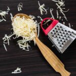 1-2 Taste Trigona - Vegan Cheese Grated in wooden spoon with grater on dark wooden table