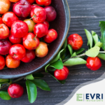 1-2 Taste EVRI Ingredients - Acerola soluble dry extract 25 - 100030 shown as fresh acerola cherries in a rustic bowl with leafy branches on a wooden surface