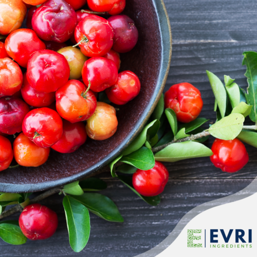 1-2 Taste EVRI Ingredients - Acerola soluble dry extract 25 - 100030 shown as fresh acerola cherries in a rustic bowl with leafy branches on a wooden surface