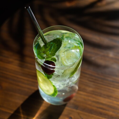 1-2 Taste Aroma INC - Natural Cucumber Elderflower Flavour - O20232 shown as Refreshing drink with cucumber slices, ice cubes, and mint in a clear glass on wooden table