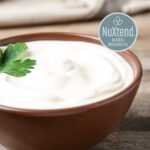 1-2 Taste NuTek Natural Ingredients - NuXtend (Cultured Wheat Flour) - NuXtend 110 in brown bowl, creamy white cultured wheat flour base with fresh green leaf garnish, showcasing clean-label food preservation
