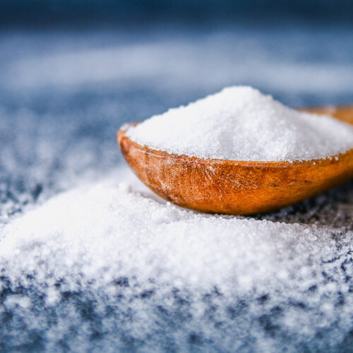 1-2 Taste NuTek Natural Ingredients - Beyond Sea Salt 85 Standard - 52850 shown as fine white salt crystals in a wooden spoon with scattered salt grains on a textured surface