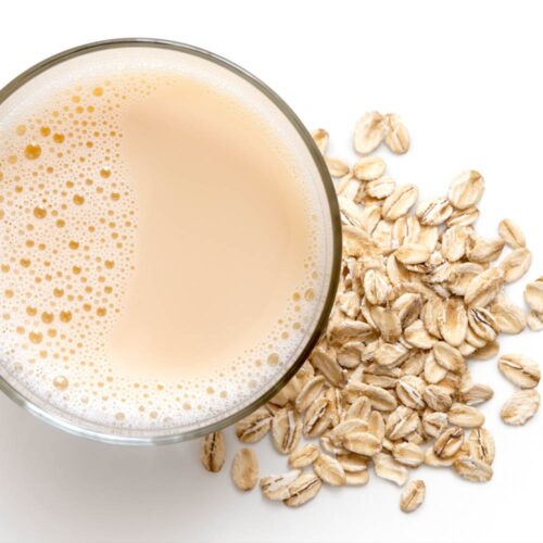 1-2 Taste Vegan Stock - Organic Gluten Free Oat Drink Powder - OGFODPEU100 shown as glass of creamy oat beverage with oat flakes on white background