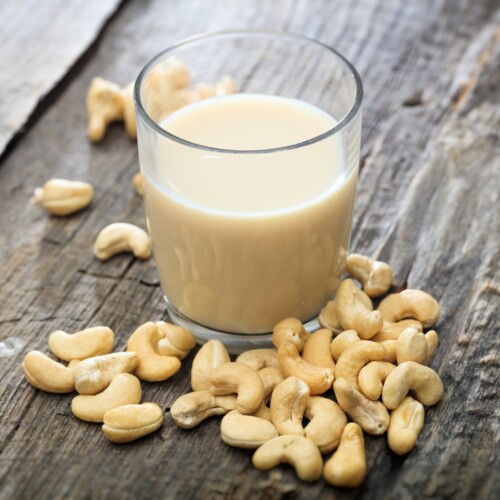 1-2 Taste Vegan Stock - Raw Cashew Milk Base - RCPEU104.A9 shown as a glass of creamy cashew milk with raw cashew nuts on rustic wooden surface