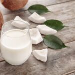 1-2 Taste Vegan Stock - Vegan Coconut Milk Powder - VCMPVN64 shown as a glass of coconut milk with coconut chunks and green leaves on rustic wooden surface